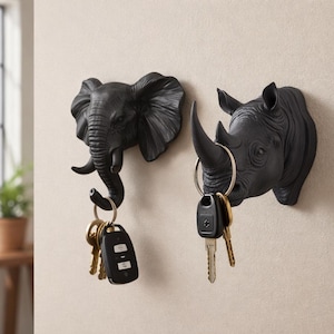 Może przedstawiać: Dwa czarne, montowane na ścianie wieszaki na klucze w kształcie słonia i nosorożca. Słoń ma zakrzywioną trąbę, która służy jako haczyk, a nosorożec ma róg. Każdy trzyma zestaw kluczy.