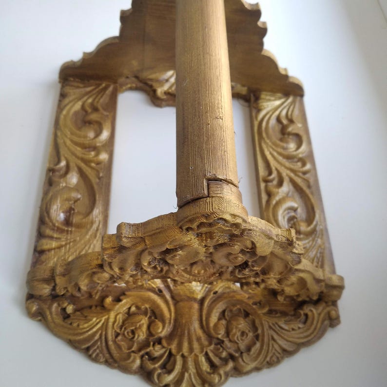 May include: A golden-coloured, ornate wooden wall shelf with a central vertical support. The shelf features intricate carved floral and scrollwork designs. The shelf is mounted on a white wall.