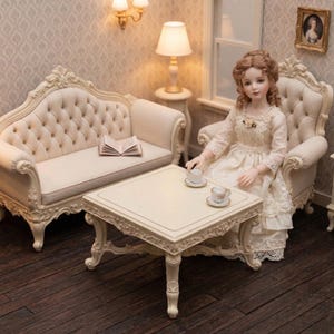 Könnte beinhalten: Eine Miniatur-Puppenhaus-Wohnzimmerszene mit cremefarbenen Möbeln. Eine Puppe in einem weißen Kleid sitzt an einem Tisch mit Teetassen. Ein Sofa und ein kleiner Tisch mit einer Lampe sind ebenfalls vorhanden. Der Raum hat eine Vintage-Ästhetik.