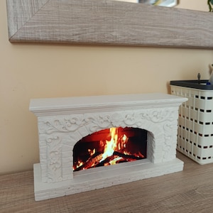 May include: A white decorative fireplace mantel featuring intricate floral carvings and a brick-patterned archway. The center opening displays a realistic, illuminated image of a burning fire with bright orange and yellow flames over dark logs.