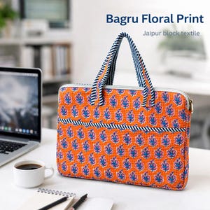 以下が含まれることがあります： 青とピンクの花柄のオレンジ色のラップトップバッグ。バッグにはジッパー開閉とストライプのハンドルが付いています。「Bagru Floral Print」と「Jaipur block textile」の文字が見えます。