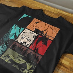 May include: Black t-shirt featuring a colorful comic-style graphic. The design includes panels with characters and a bear. The shirt is made of a soft material and is suitable for casual wear.