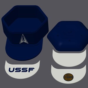 May include: Navy blue hat with a white logo and the text "USSF". The hat has a hexagonal crown and a curved brim. The hat is accompanied by a matching top and two white semi-circles with text.