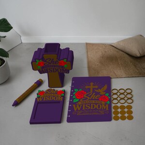 May include: A purple desk set featuring a cross-shaped pen holder, a notepad holder, a notebook, and a pen. Each item displays red roses and the text "She speaks with wisdom" in gold lettering. Includes a set of gold-coloured circular rings.