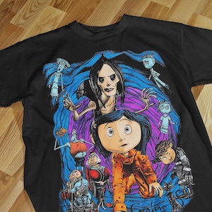 Puede incluir: Camiseta negra con un gráfico colorido de la película "Coraline". El diseño presenta personajes como Coraline, la Otra Madre y otras figuras en tonos azules, morados y naranjas. La palabra "Coraline" está en la parte inferior.