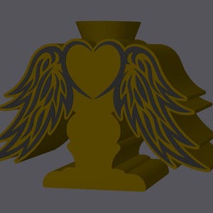 May include: A gold-coloured decorative object featuring a heart shape in the centre, flanked by stylised wings. The wings have a dark grey outline. The object has a base and a cylindrical top, possibly for holding an item. The design is symmetrical and three-dimensional.