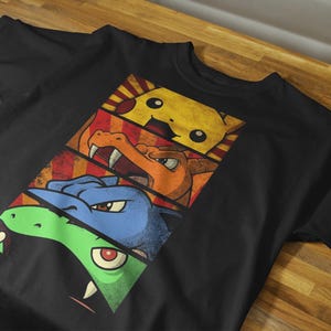 May include: Black t-shirt featuring a graphic design of three cartoon characters in separate panels. The top panel shows a yellow character, the middle panel shows an orange character, and the bottom panel shows a blue and green character.