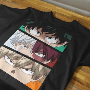 May include: Black t-shirt featuring a graphic of three anime character faces. Each face is in a separate rectangular panel with different colored backgrounds. The characters have distinct eye colors and hairstyles.