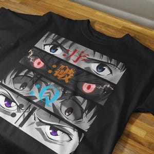 May include: Black t-shirt featuring a graphic design of anime eyes in various styles and colors. The design includes Japanese text in red and orange. The eyes have blue, red, and purple irises.