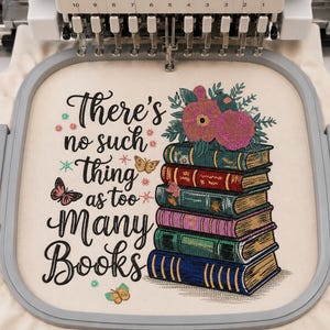 May include: An embroidery design on off-white fabric in a gray hoop featuring a stack of five colorful books topped with pink flowers. The text reads, There's no such thing as too many books, accompanied by small embroidered butterflies and star accents.