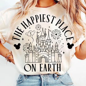 Puede incluir: Una camiseta blanca con un gráfico negro del castillo de Cenicienta y el texto "The Happiest Place on Earth".