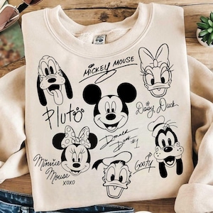 May include: A beige sweatshirt with black and white illustrations of Mickey Mouse, Minnie Mouse, Donald Duck, Daisy Duck, Goofy, and Pluto. The characters are drawn in a cartoon style and have their names written next to them.