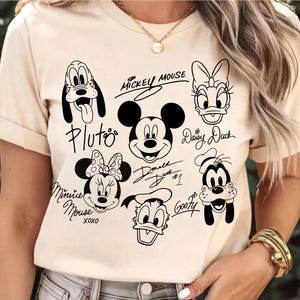May include: A white t-shirt with black cartoon images of Mickey Mouse, Minnie Mouse, Donald Duck, Daisy Duck, Goofy, and Pluto. Each character has their name written in cursive underneath their image.