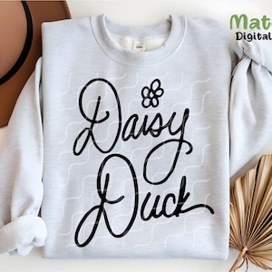 Puede incluir: Una sudadera blanca con un dise&ntilde;o gr&aacute;fico negro que dice "Daisy Duck" con una peque&ntilde;a flor sobre la palabra "Daisy".