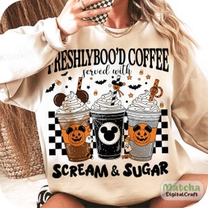 May include: Cream-coloured sweatshirt with a Halloween graphic. The design shows three coffee cups with whipped cream, pumpkins, and the text "FRESHLYBOO'D COFFEE served with SCREAM & SUGAR". Bats and candy corn are also included.