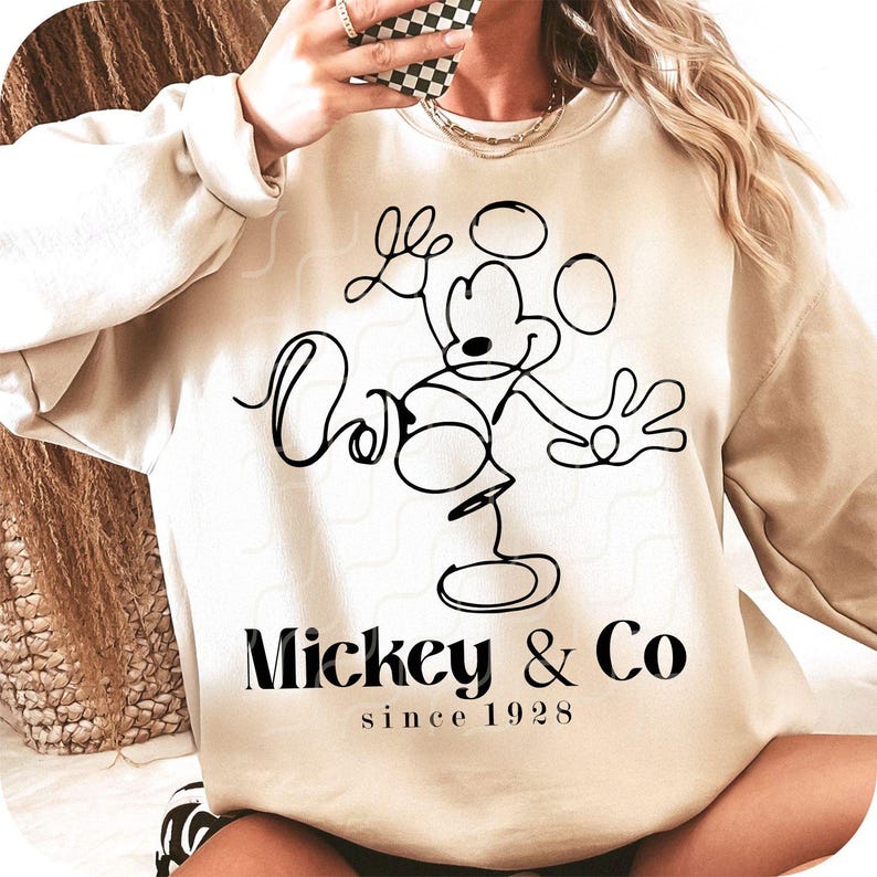 May include: A beige sweatshirt with a black outline drawing of Mickey Mouse and the text "Mickey & Co since 1928".