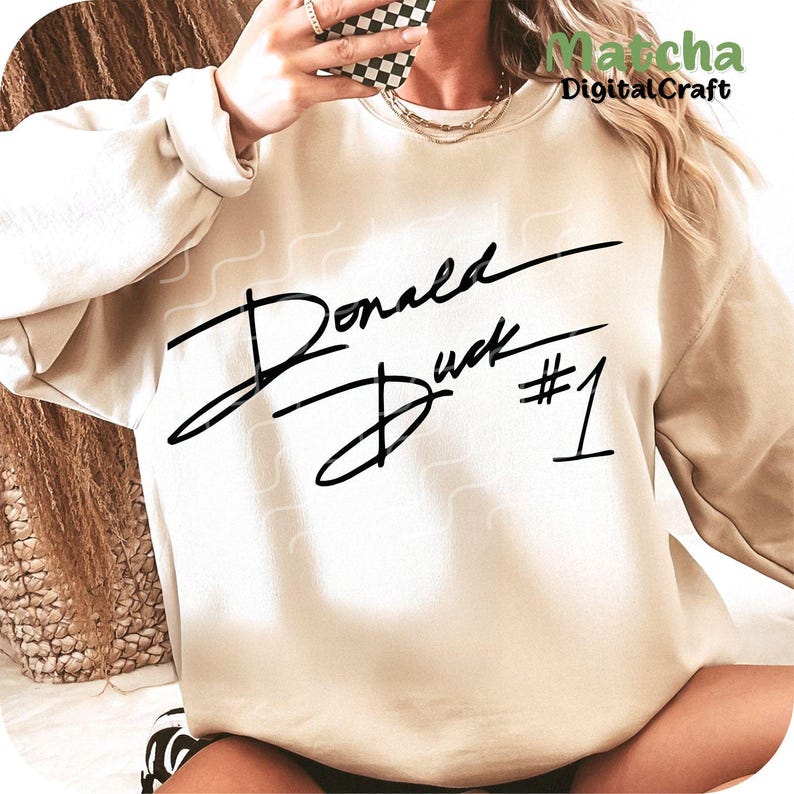 Puede incluir: Una sudadera beige con un estampado gr&aacute;fico negro de la firma "Donald Duck #1".