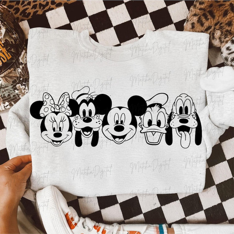 May include: A light gray sweatshirt featuring a black and white graphic of Disney characters: Minnie Mouse, Goofy, Mickey Mouse, Donald Duck, and Pluto. The sweatshirt is displayed on a black and white checkered surface.