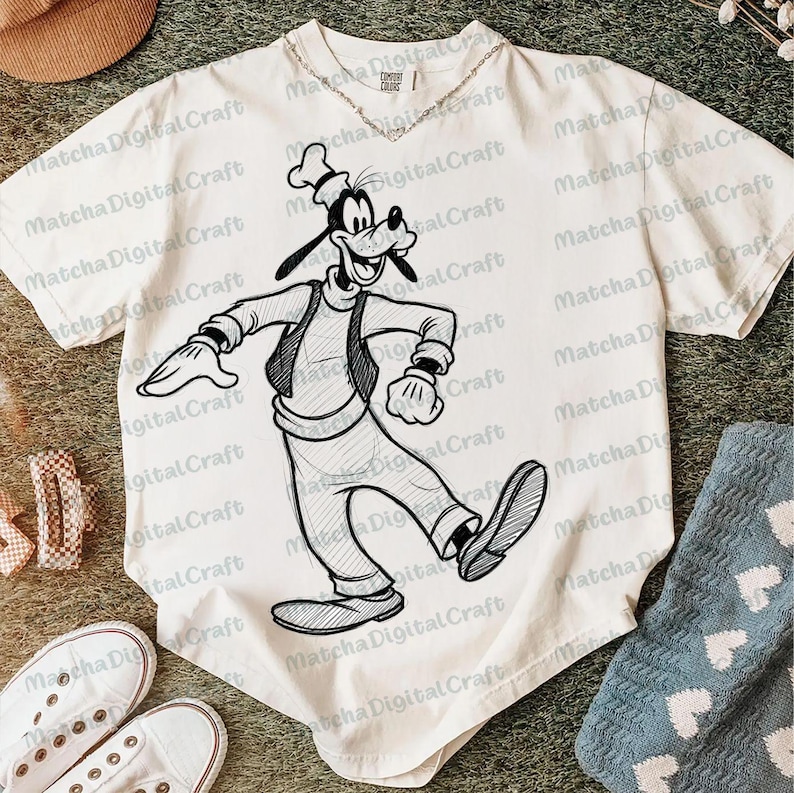 K&ouml;nnte beinhalten: Cremefarbenes T-Shirt mit einer Schwarz-Wei&szlig;-Skizze von Goofy in Bewegung. Das Shirt hat einen Rundhalsausschnitt und kurze &Auml;rmel. Eine silberne Halskette ist sichtbar. Der Text "Matcha Digital Craft" ist auf dem Shirt aufgedruckt.