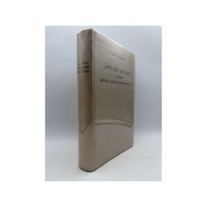 May include: A hardcover book titled "Apes and Ape Lore" by W.W. Janson. The book has a light beige cover with the title and author's name printed in dark text. The book is standing upright.