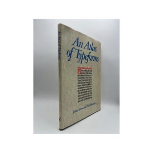 May include: A cream-colored book with a blue title, "An Atlas of Typeforms" by James Sutton and Alan Bartram. The book cover features a small red symbol in the upper right corner.