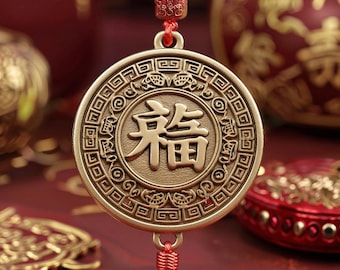 May include: A gold-colored circular pendant with the Chinese character for "blessing" in the center. The pendant is adorned with intricate patterns and hangs from a red cord with a tassel. The background features other decorative items.