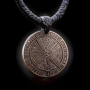 Può includere: Una collana con un ciondolo rotondo in bronzo decorato con simboli e motivi intricati. Il ciondolo è sospeso da un cordoncino intrecciato nero.