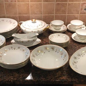 Puede incluir: Un juego de vajilla completo de porcelana blanca vintage con ribete dorado y un delicado estampado floral. Incluye platos, cuencos, tazas, platillos, una fuente para servir, una salsera, una fuente cubierta y una azucarera.