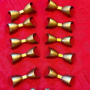 May include: A collection of eleven brass-toned metal drawer pulls, each shaped like a bow with curved ends. Ten pulls are arranged in two vertical columns, while one pull is positioned at the bottom, displaying two attached metal mounting screws.
