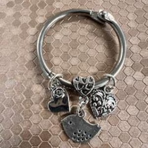 Peut inclure: Bracelet en argent avec des breloques en forme d'oiseau, de cœur et de fleurs.