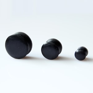 May include: Three black wooden ear gauges of different sizes. The gauges are round and have a smooth, polished finish.