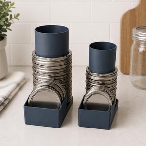 Peut inclure: Deux organisateurs en plastique bleu foncé contenant des piles de couvercles et de bagues de bocaux en métal argenté. Chaque organisateur comporte un support cylindrique vertical pour les bagues et un compartiment rectangulaire pour les couvercles.