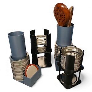 May include: A collection of kitchen organizers in various designs. The organizers are in shades of gray and black, holding jar lids, lids, and wooden cooking utensils. The items are arranged on a white background.
