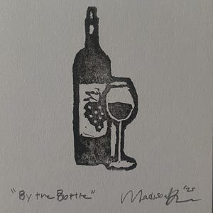 May include: A black ink block print on white paper featuring a wine bottle with a grape cluster graphic and a stemmed wine glass. The text "By the Bottle" is printed in the lower left corner, with a handwritten signature and the year '25 on the right.