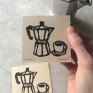 May include: Two black and white linocut prints of a coffee pot and a cup of coffee. The prints are signed and numbered. The text on the prints reads "Moka Pot".