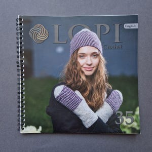 Op de afbeelding: Een tijdschriftcover met een vrouw die een paars-wit gestreepte muts en bijpassende wanten draagt. Het tijdschrift heet "LOPI Crochet" en het nummer is 35. Het tijdschrift is in het Engels.