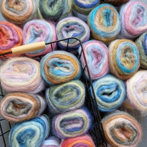 以下が含まれることがあります： カラフルな糸玉が詰まったバスケットのクローズアップ。糸は柔らかくふわふわで、さまざまな色とパターンがあります。糸玉は円形に配置され、視覚的に魅力的なディスプレイになっています。