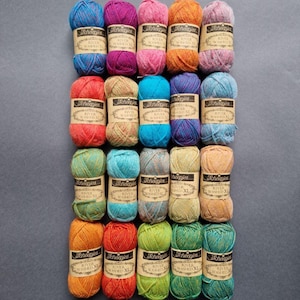 May include: A selection of multi-coloured yarn skeins, each with a label reading "Scheepjes River Washed XL." The yarn is in shades of blue, pink, orange, green, and brown, arranged in neat rows, ideal for knitting or crochet.