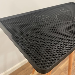 May include: A black, textured table with a geometric pattern and the word "LOVE" etched into the surface. The table has a rectangular shape with rounded corners and is supported by three light-colored wooden legs.
