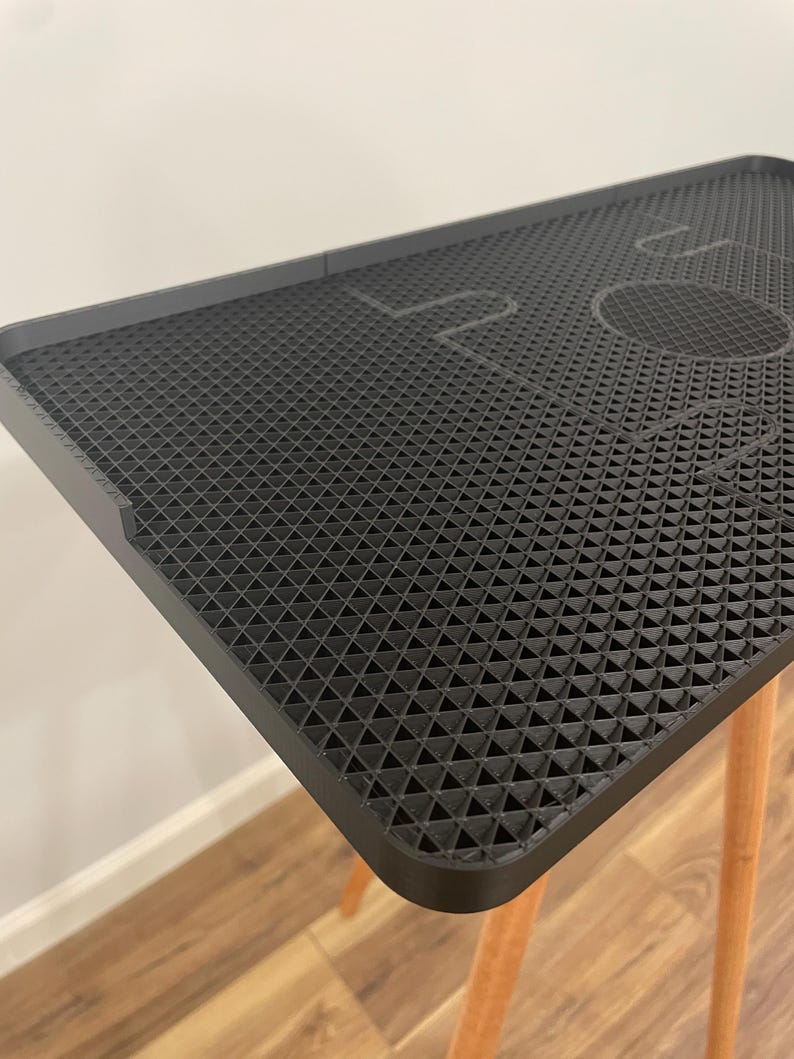 May include: A black, textured table with a geometric pattern and the word "LOVE" etched into the surface. The table has a rectangular shape with rounded corners and is supported by three light-colored wooden legs.