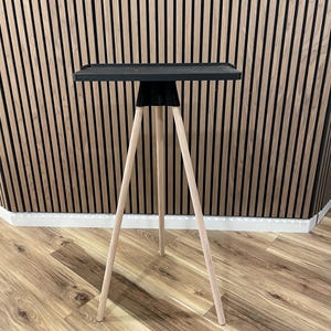 May include: A modern side table with a black square top and three light-colored wooden legs. The legs are angled outward for stability. The table is designed for indoor use and has a minimalist aesthetic.