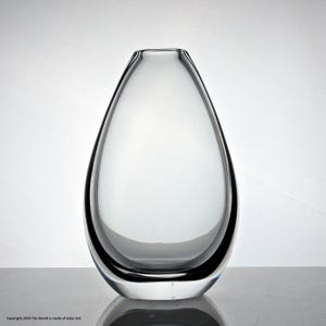 Könnte beinhalten: Eine klare Glasvase in Tropfenform. Die Vase hat eine breite Öffnung oben und einen schmalen Boden.