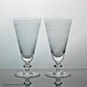 May include: Two clear glass goblets featuring a delicate, etched swirling pattern across the upper bowls. Each glass has a tapered shape, a multi-tiered stem, and a circular base. The text "Copyright 2024 The World is made of Glass Ltd." is visible.