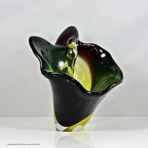 May include: A handcrafted art glass vase with a unique, organic shape. The vase features a blend of colors, including black, green, yellow, and burgundy. The design is asymmetrical, with a flared rim and a smooth, glossy finish. The vase is a decorative piece.