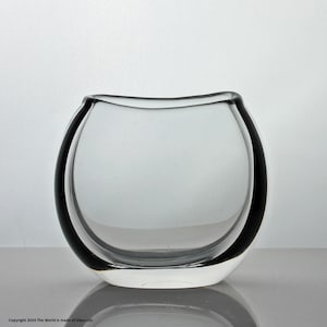 Könnte beinhalten: Eine klare Glasvase mit abgerundeter, leicht geschwungener Form. Die Vase hat einen schwarzen Rand und eine breite Öffnung.