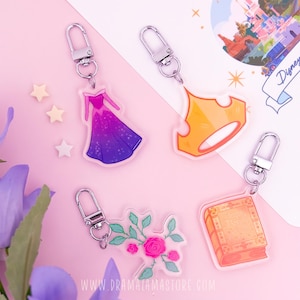 May include: Four acrylic keychains featuring a pink and purple ombre gown, a gold crown, a pink rose floral arrangement with green leaves, and an orange book titled Sleeping Beauty, each attached to a silver metal lobster clasp hook.