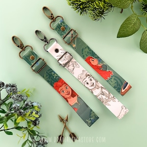 Puede incluir: Tres correas decorativas para bolsos con diseños de personajes de dibujos animados. Dos correas son verdes con estampados florales e ilustraciones de personajes. La tercera correa es blanca con una ilustración de personaje en blanco y negro. Cada correa tiene un cierre y una hebilla metálicos.