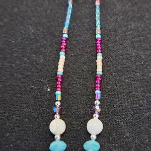 May include: A beaded eyeglass chain with a variety of colorful beads. The chain features small, iridescent beads in shades of pink, blue, and green. Larger beads are white, turquoise, and silver. The chain is designed to hold eyeglasses.