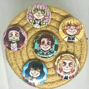 May include: Seven round button badges featuring anime characters. Each badge displays a different character with bright colours and detailed facial expressions. The badges are arranged on a woven, circular coaster.
