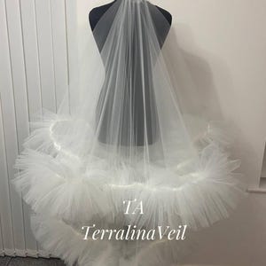 Puede incluir: Un velo de novia de tul blanco con un borde con volantes. El velo está en un maniquí y el texto "TA Terralina Veil" es visible.